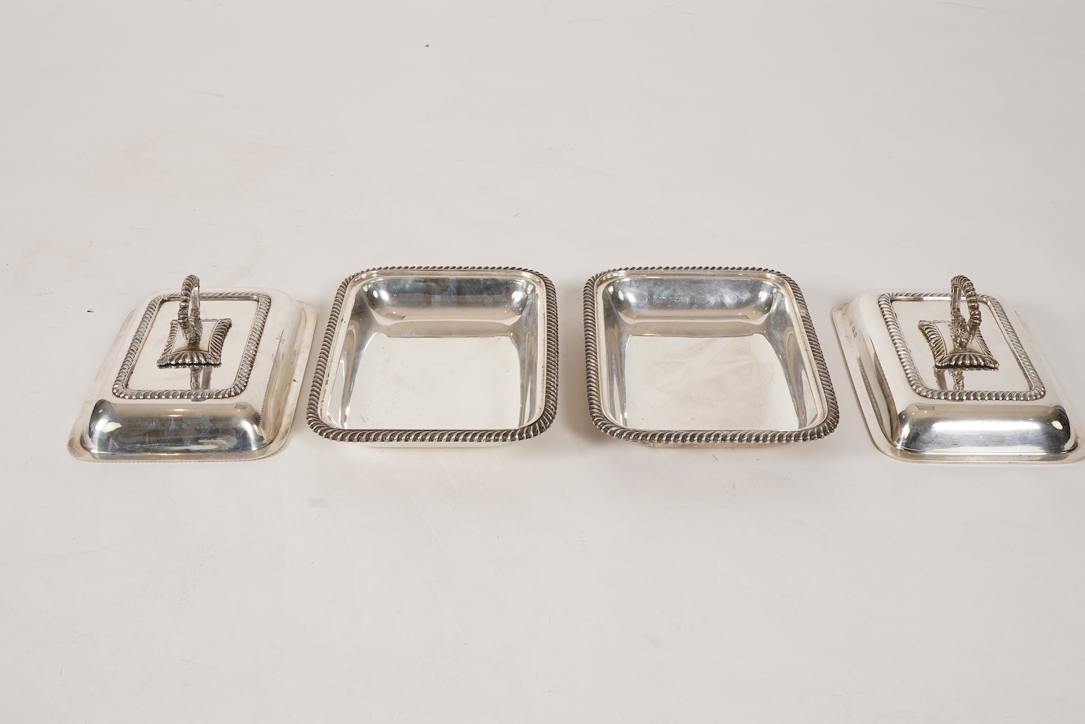 A matched pair of George V silver rectangular entrée dishes and covers, both with gadrooned borders and similar unmarked handles, Ellis & Co, Birmingham, 1923 and Ellis & Co, Birmingham, 1932, base 27.8cm, 108.3oz, exclu